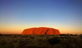 Uluru Ayers Rock by sunset. Evening dark blue sky with natural orange sunlight.
